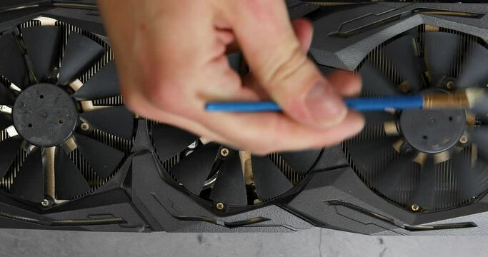 close-up of unrecognizable computer master wiping cooler blades of modern gaming graphics card