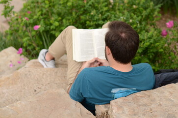 close up of a young white guy sitting on a rock in a park and reading a book in solitude...