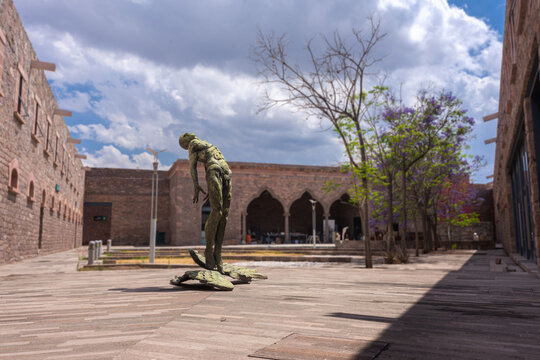 Outdoor secondary courtyard, stone architecture with statue at the center of a naked man looking up at the sky inside the Leonora Carrington Museum, no people