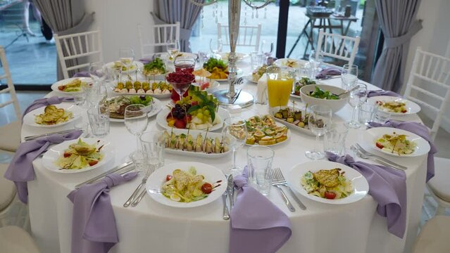 Round table of appetizers and portion salads with clean cutlery and lavender napkins with chiavari chairs. Bright banquet hall in front of official reception.