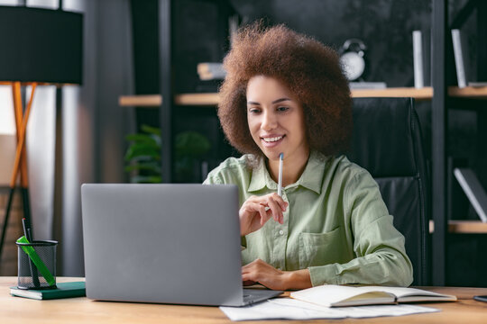 Young beautiful joyful business woman smiling while working with laptop sitting at the workplace in modern office