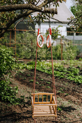 A children's homemade wooden swing made of boards hangs on a rope outdoors in the backyard garden. Closeup photo, childhood concept.