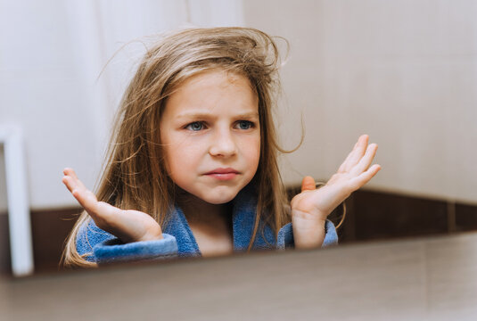 Beautiful funny smiling girl in bathrobe, child grimaces looking in the mirror in the bathroom in the morning. Photography, portrait.