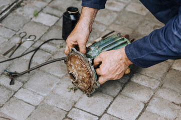 Elderly male professional worker, electrician, electromechanic repairs an old rusty electric motor...
