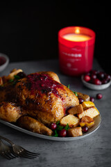 Roasted whole chicken with cranberry sauce. Dark background with Christmas candle. Christmas food.