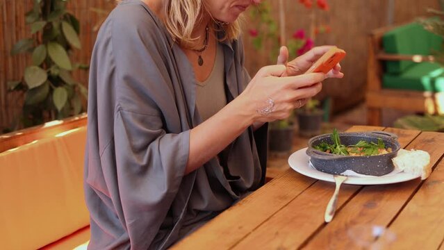 Side view of a stylish hippie woman blogger taking picture of her food in a cafe, woman hands make video of her beautifully served omlette