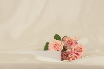 Pink rose flower bouquet on white podium and silk fabric.. Light beige background. Minimal empty...