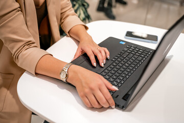 A business woman sits in a cafe and works at a computer. She is wearing a beige jacket.