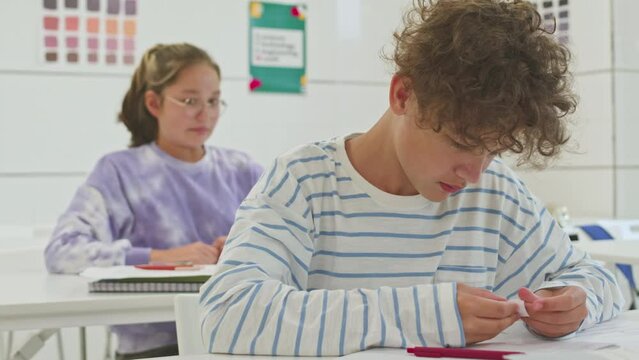 Waist up of preteen schoolgirl passing cheat sheet to her classmate during exam