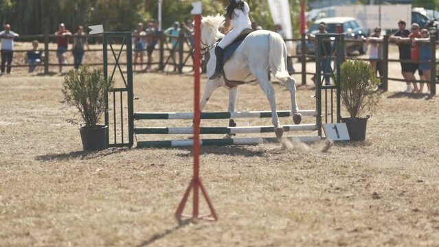 Equestrian sport - riding a white horse at the arena - jumping over a barrier
