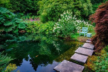 A chair and table await in a beautiful serene garden by a pond with fish