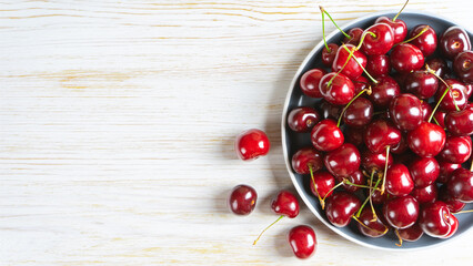 Fresh red ripe sweet cherry on plate on white wooden background. Berry, food background. Top view, banner, header with copy space.