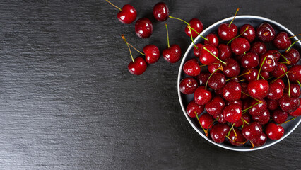 Fresh red ripe sweet cherry with water drops on plate on black slate, stone background. Berry, food background. Top view, banner, header with copy space.