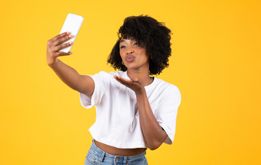 Happy young african american curly lady make blowing kiss and selfie on smartphone, have fun