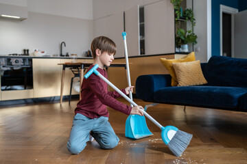 Little boy sweeping floor in living room, kid doing daily regular household chores and helping...