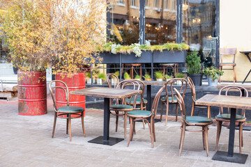 Fototapeta na wymiar Empty cafe with terrace with tables and wooden chairs. Street vintage exterior of restaurant. Furniture for coffee shop in street in Europe. Typical view of Parisian street with tables of cafe 