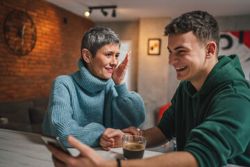teenage boy and mature caucasian woman sit together at the kitchen at home talk mother and son or relatives support solving problem share experience and opinion boy hold mobile phone smartphone