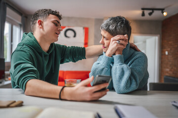 teenage boy and mature caucasian woman sit together at the kitchen at home talk mother and son or...