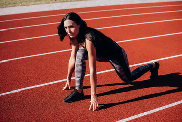 Full body side view of focused young female sprinter in low start position ready to run from...