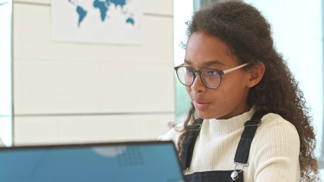 Chest up of pretty African American schoolgirl chatting with classmates in class