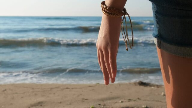 Girl with stylish bracelet by sea. A young girl with stylish bracelet pass her time on the sandy shore against ocean bay during summer trip.