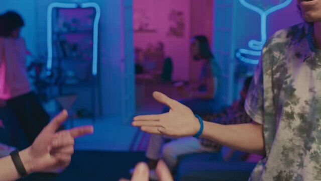 Close-up slowmo shot of hands of two unrecognizable casually dressed young men, with rings and bracelets, greeting each other at house party, bumping fists and gesticulating