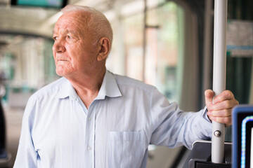 Old European man standing in streetcar and waiting for next stop.