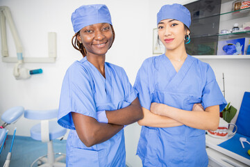 Two dentists in the dental office pose together smiling with their arms folded