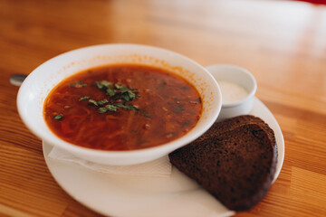 Traditional Ukrainian borsch. White Bowl of red beet root soup and greens. Sour delicious soup with potato, meat, carrot, cabbage, garlic. Traditional Ukraine food cuisine with brown bread, sour cream