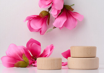 Empty round wooden platform and branches with pink magnolia flowers on a white background. Place for demonstration of products, cosmetics