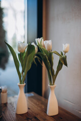 Graceful bouquet of tender white tulips. Light vintage vase with bunch of flowers is located on the table .  Art photography.