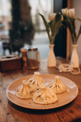 4  Khinkali on the plate in cafe. Blurred bouquet of tender white tulips. Light vintage vase with bunch of flowers is located on the table . .