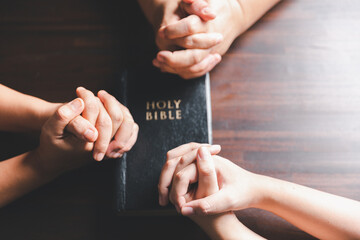 Christian small group praying together around a wooden table with bible page in homeroom. Christian...