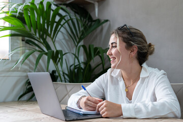 Portrait of smiling millennial caucasian female student sit at desk at home study online on laptop. Happy young cheerful woman use computer take distant course or training. Education concept..