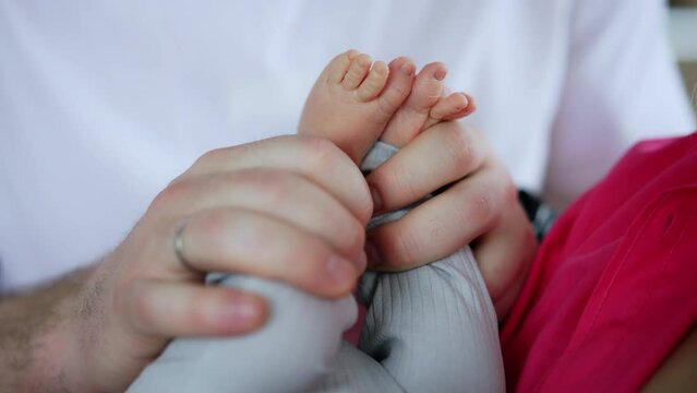 Big male Caucasian hands holding tiny baby feet. Happy father kisses son's feet and puts them on a face. Close up.