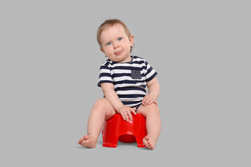 Little child sitting on baby potty against light grey background