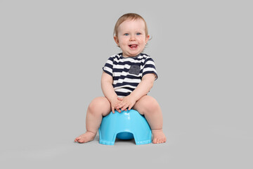 Little child sitting on baby potty against light grey background