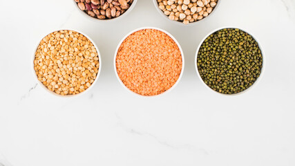 Legumes in glass jars top view on white background. Vegetable protein, healthy eating. Copy space