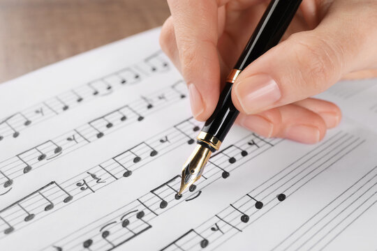 Woman writing musical notes with fountain pen on sheet of paper, closeup