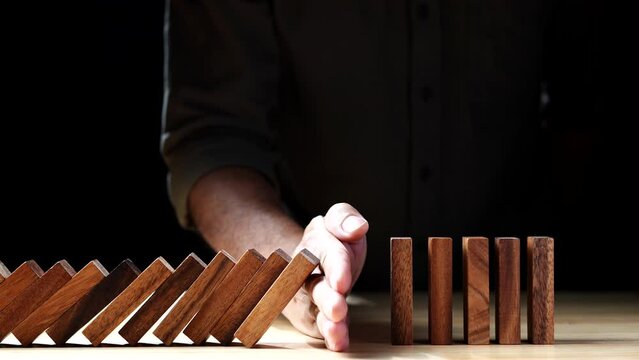 Close up Businessman hand stopping wooden domino business crisis effect or risk protection on dark background. Concept of Risk, Management, Assessment, Business, Crisis, Financial, Planning, Economic