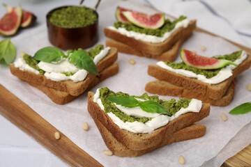 Tasty bruschetta with cream cheese, pesto sauce and fresh basil on parchment paper, closeup