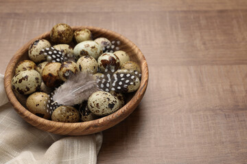 Speckled quail eggs and feathers on wooden table, space for text