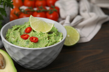 Obraz premium Bowl of delicious guacamole and ingredients on wooden table, closeup. Space for text