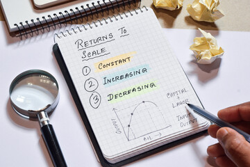 Kinds of Returns to scale, constant increasing and decreasing explanation handwritten on notepad for presentation. Selective focus.
