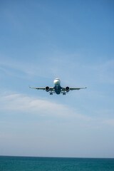 Fototapeta na wymiar A plane is landing near white beach and blue sky.