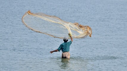 Man in blue shirt and gray shorts throwing a fish net in water