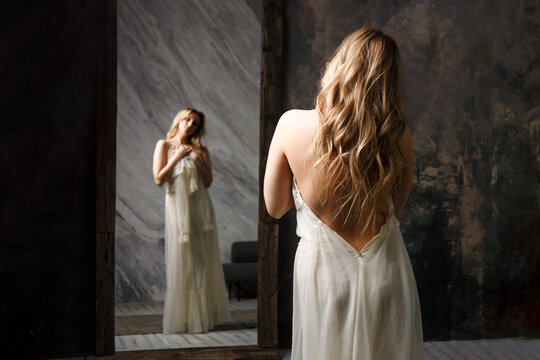 Blonde Woman in white dress looking at reflection in mirror