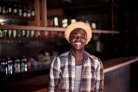 Man wearing hat and plaid shirt smiling in front of bar