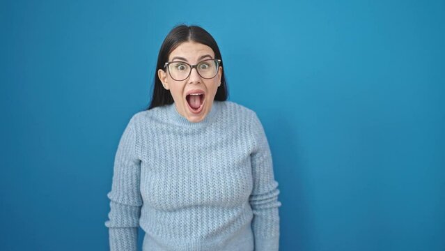 Young hispanic woman standing with happy surprise expression with hands on mouth over isolated blue background