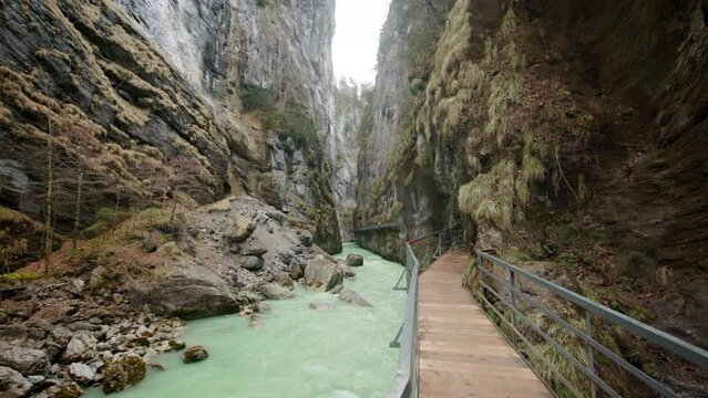 Camera slides through the scenic wooden bridge near emerald creek, embraced by majestic mountains and serene rock formations in the enchanting Aare Gorge, Switzerland. High quality 4k footage.